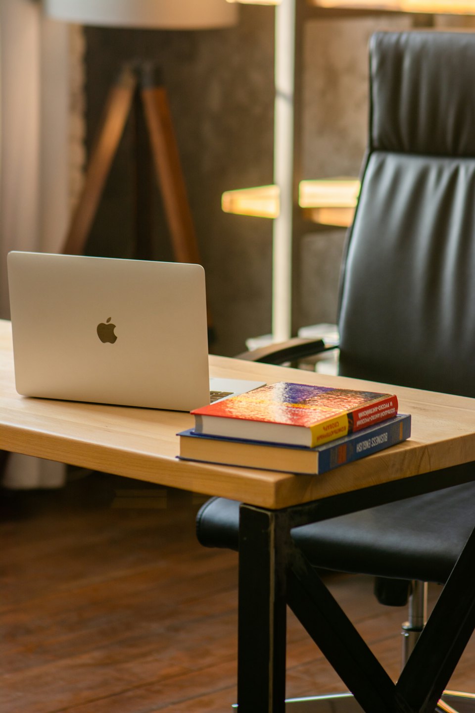 Silver laptop and books on a wooden desk.