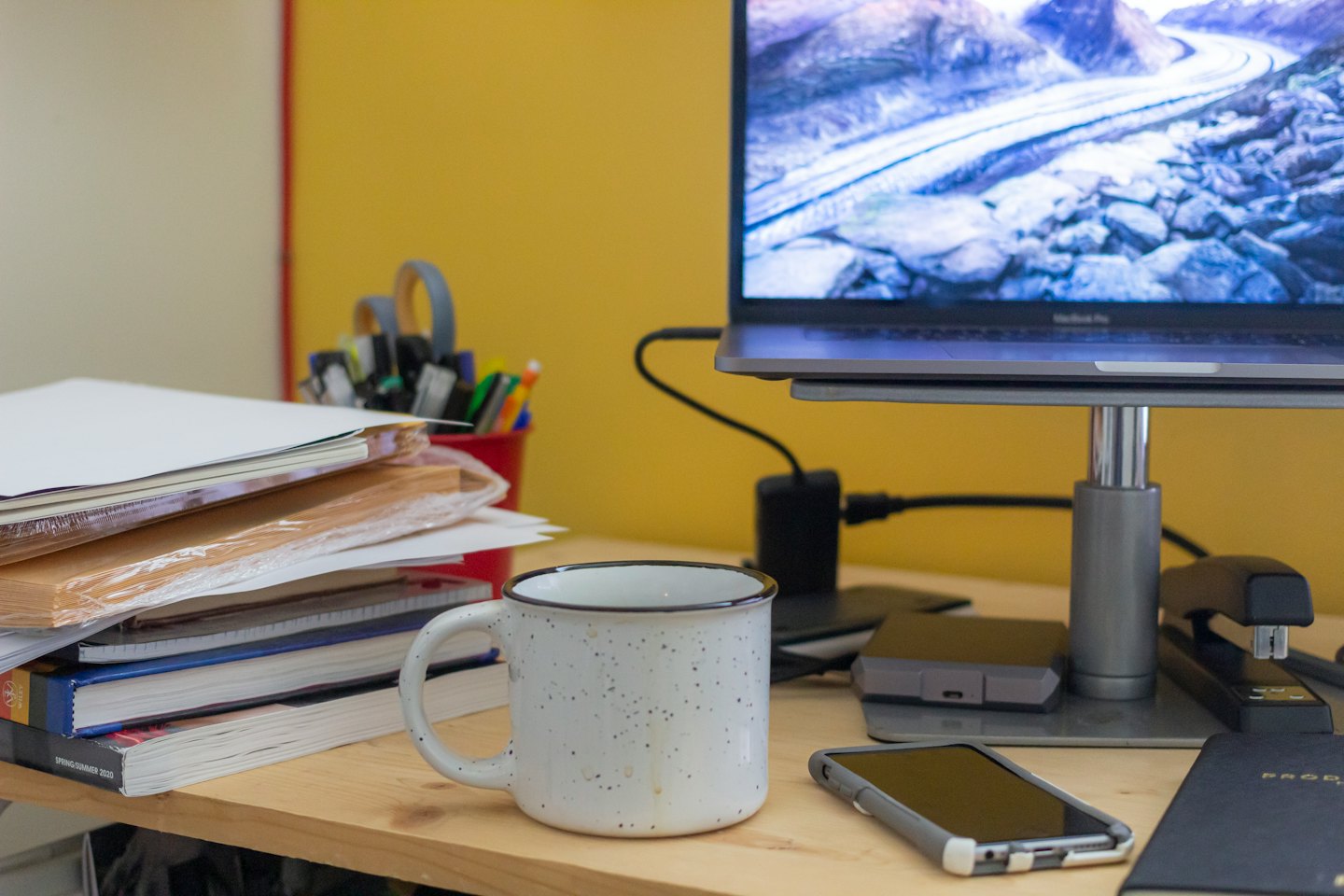 Laptop and office supplies on a wooden desk with yellow wall.